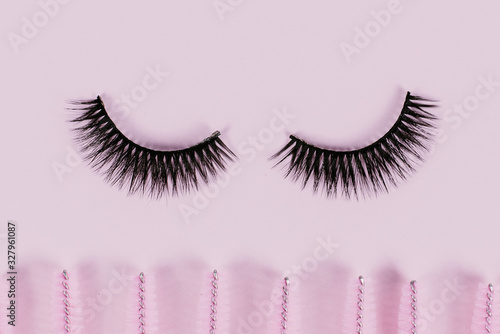 Black fake ribbon eyelashes and brushes for combing extension eyelashes on a pink trendy pastel background. False eyelashes, applicator and brushes. Beauty shop. Makeup cosmetics. Top view, flat lay