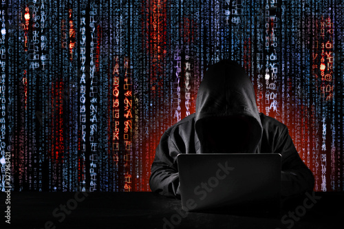 Dangerous anonymous hacker man in black hooded using computer, breaking into security data corporate server. He working on digital binary and matrix code. Internet crime, cyber attack security concept