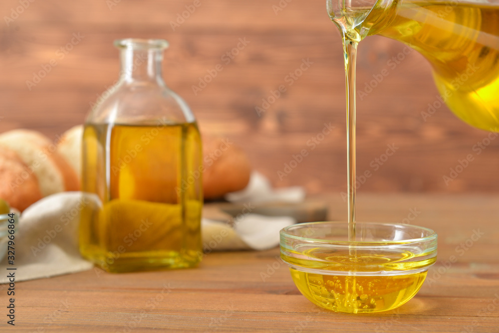 Pouring of tasty olive oil from bottle into bowl on table Pouring of tasty olive oil from bottle into bowl on table