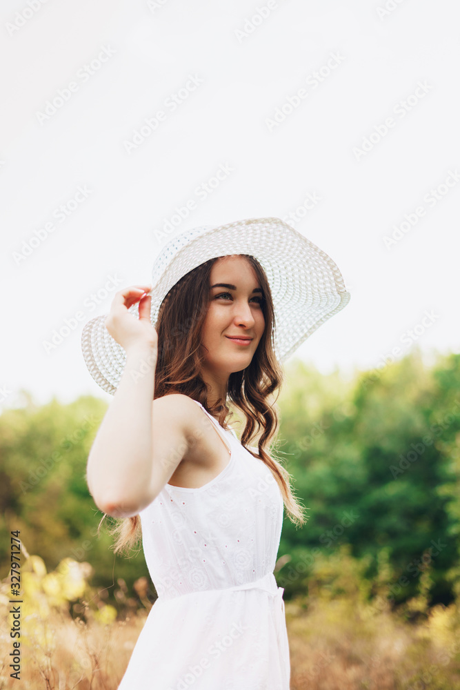 Portrait of a beautiful smiling young woman in light white dress and hat in the summer park. Beauty, fashion. Holidays.