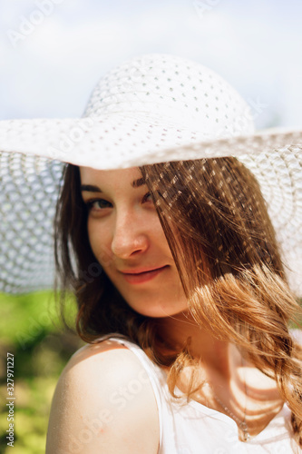 Portrait of a beautiful smiling young woman in light white dress and hat in the summer park. Beauty, fashion. Holidays.