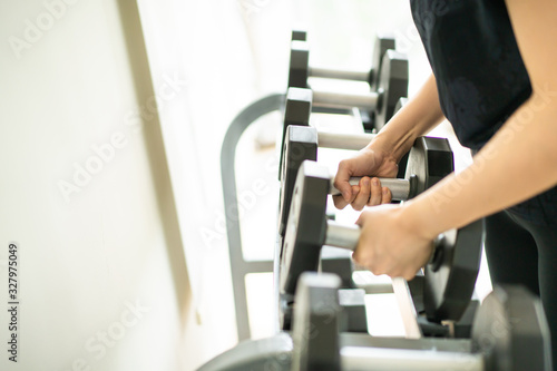 Sport woman picking up a dumbbells from dumbbell rack.