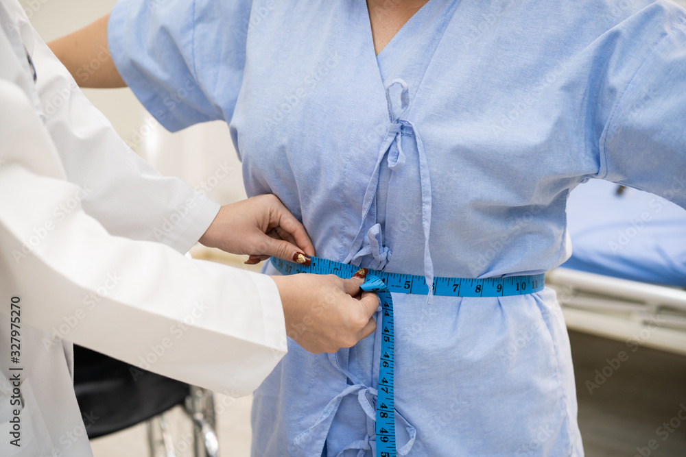 Asian woman doctor measuring a big stomach of fat woman by using tape