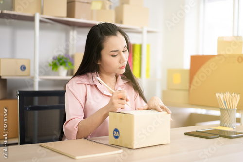 Young Asian business woman packing a post boxes to be shipped to customers. Ecommerce online shopping concept. Expertise online sales person packing customers parcel boxes for shipment.