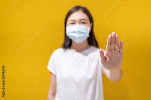 Asian young attractive woman wearing a protective hygiene mask over her face to protect flu and virus. Unwell influenza in infected woman portrait with yellow background. Covid19 and Coronavirus.