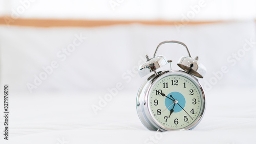 Retro vintage style analog alarm clock on the white bed close up with copyspace. Asleep and exhausted working people in the morning. Retro analog alarm clock almost 7 O'Clock.