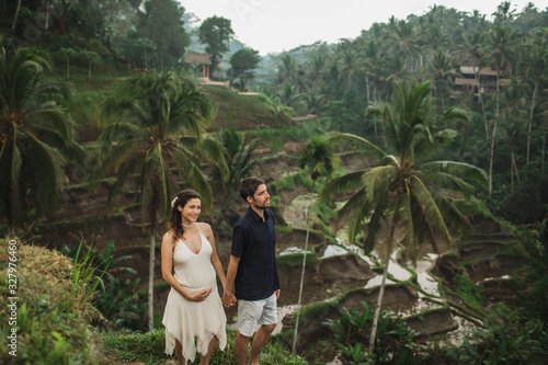 Young latin pregnant woman with husband with amazing view of Ubud rice terraces. Pregnant couple happy together.