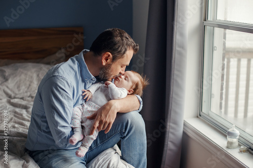 Middle age Caucasian father kissing sleeping newborn baby girl. Parent holding rocking a child daughter son in hands. Authentic lifestyle parenting fatherhood moment. Single dad family home life.