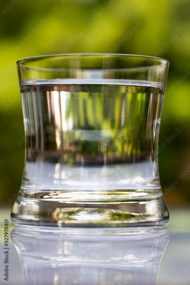 Blurred transparent glass of clean water on white table in bokeh green garden background, Close up & Macro shot, Selective focus, Healthy Drink concept Blurred transparent glass of clean water on white table in bokeh green garden background, Close up & Macro shot, Selective focus, Healthy Drink concept
