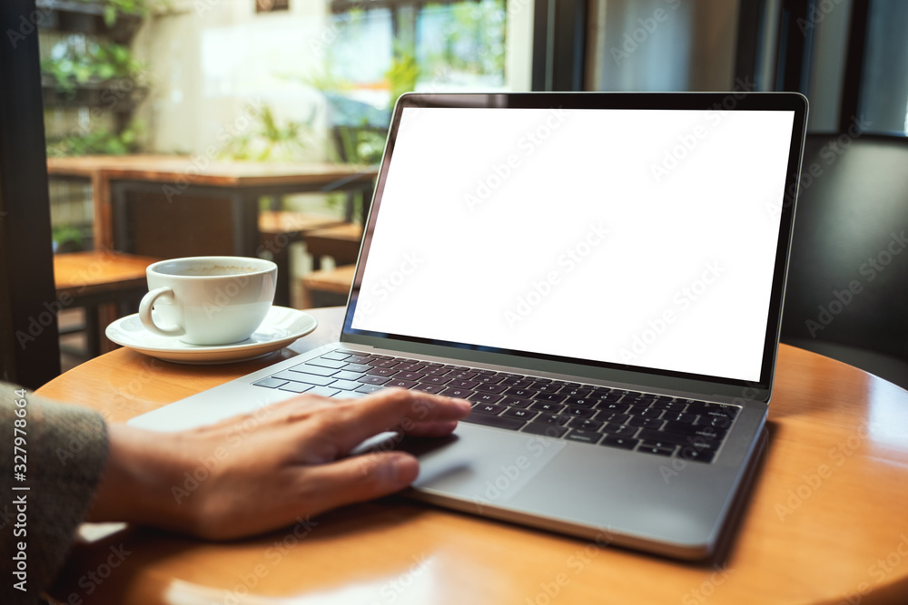 Mockup image of a woman using and touching on laptop touchpad with blank white desktop screen with coffee cup on the table Mockup image of a woman using and touching on laptop touchpad with blank white desktop screen with coffee cup on the table