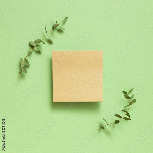 Kraft memo pad, empty paper with eucalyptus leaves on pastel green background. top view, copy space