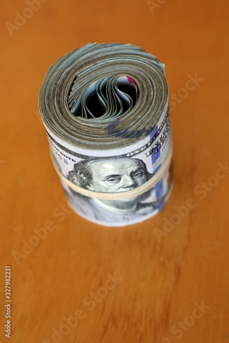 financial image of close up rolled and rubber banded American one hundred dollar bills pile on desk