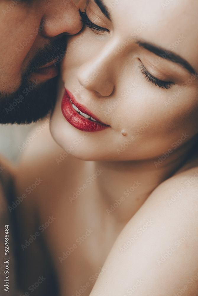 Fototapeta premium Stunning caucasian girl with red lips is kissed by her bearded lover while embracing each other