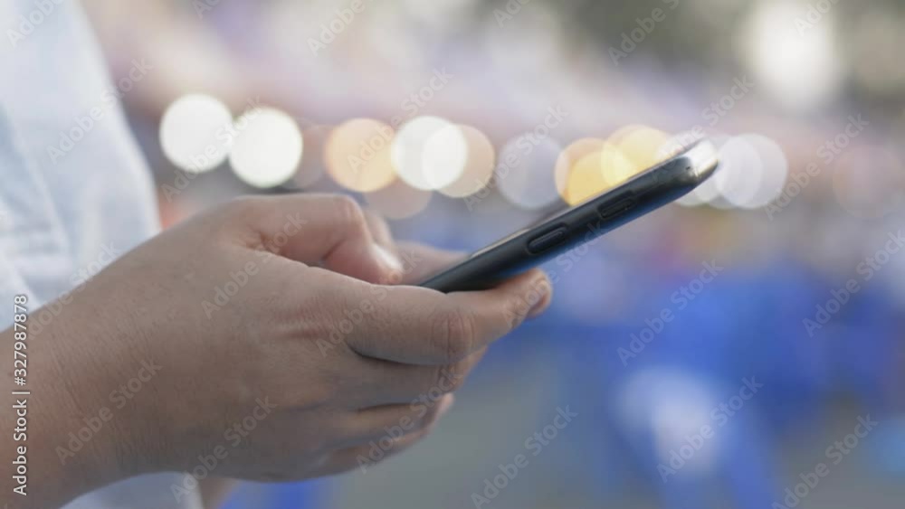 Hands of woman texting message on mobile smart phone for communication and chatting on social online at street food market in evening. Lighting bokeh background. Hands of woman texting message on mobile smart phone for communication and chatting on social online at street food market in evening. Lighting bokeh background.