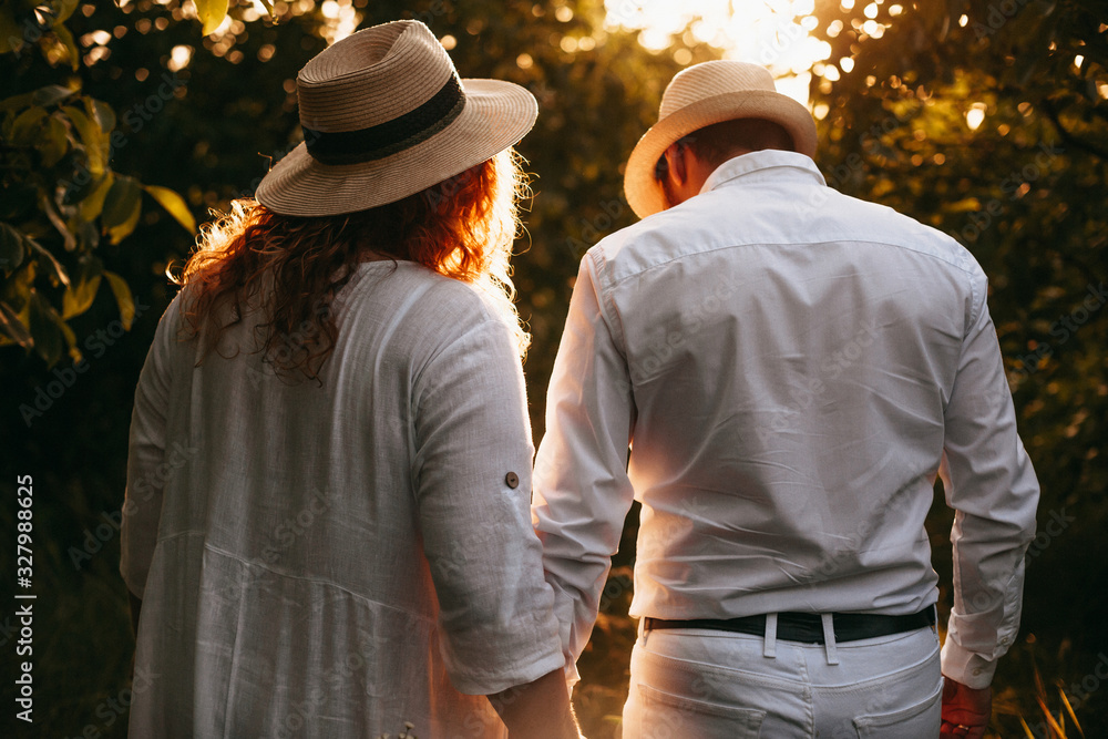 Back view portrait of a plump caucasian lady with red hair walking with her lover in a park wearing hats and while clothes