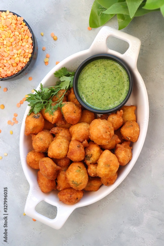 Moong dal ke pakode, ram laddoo, bhajias, Moongode or fritters. served with green mint and coriander chutney. Served over light background. Selective focus. with copy space. Moong dal ke pakode, ram laddoo, bhajias, Moongode or fritters. served with green mint and coriander chutney. Served over light background. Selective focus. with copy space.