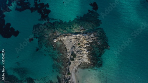 Aerial view of Vourvourou beach, small peninsula in turquoise water of Aegean sea. Waves beating cliff rocky coastline. Halkidiki, Greece.