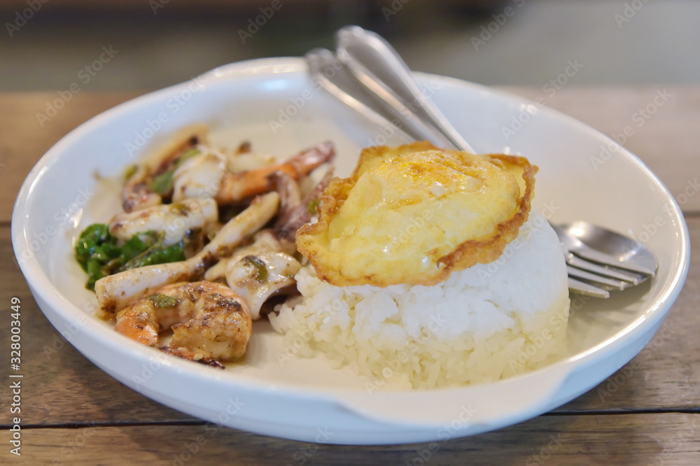 Rice topped with stir-fried seafood and basil close up shot