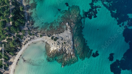 Aerial view of Vourvourou beach, small peninsula in turquoise water of Aegean sea. Waves beating cliff rocky coastline. Halkidiki, Greece.