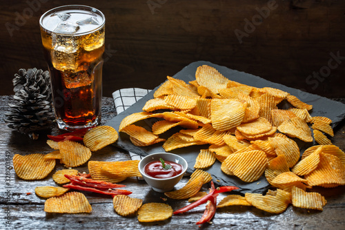 Potato chips spicy barbeque flavor on slate and wood floor with ketchup and soda drink for relaxation activity.