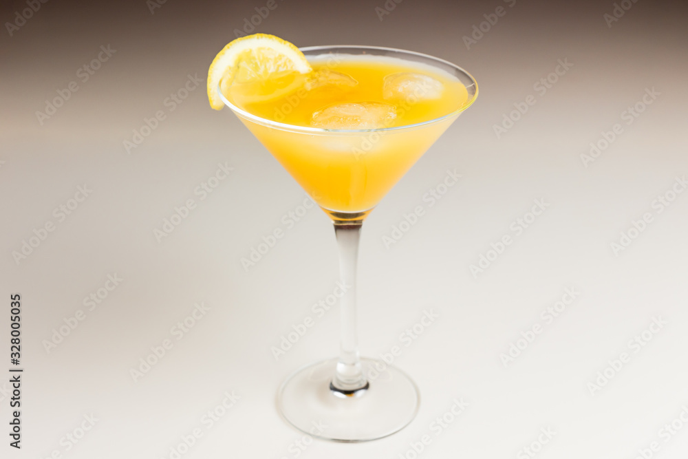 An orange cocktail with ice in a martini glass garnished with lemon