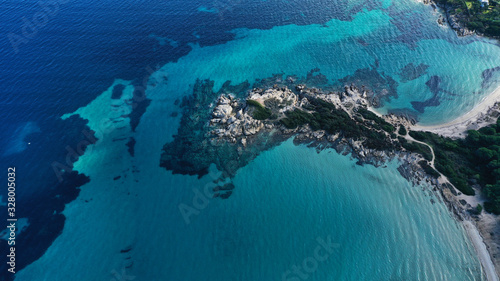 Aerial view of Vourvourou beach, small peninsula in turquoise water of Aegean sea. Waves beating cliff rocky coastline. Halkidiki, Greece.