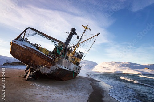 A fishing boat lying on its side, washed up by a storm on the shore of the Barents sea, the Kola Peninsula, Teriberka, Russia photo