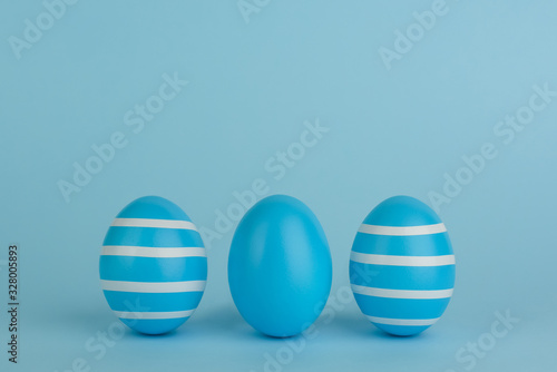  Three Easter decorated blue eggs. Striped blue eggs in a row on a blue background. White strips. Copy space. Blue monochrome.
