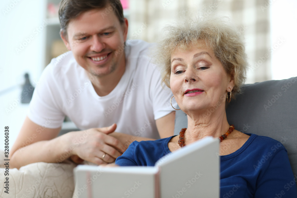 Elderly lady sits sofa watches album with her son. Productive and interesting time with an elderly mom. Adult son takes into account need for parents to communicate. Son visits mother in nursing home Elderly lady sits sofa watches album with her son. Productive and interesting time with an elderly mom. Adult son takes into account need for parents to communicate. Son visits mother in nursing home