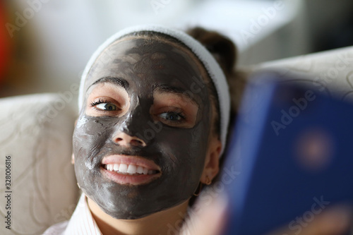 Smiling girl has black coal mask on her face. Moisturizing and soothing for quick recovery. Stimulate blood circulation, smooth surface and skin tone. Innovative high-tech ingredients photo