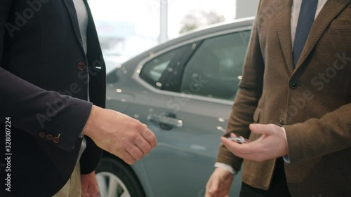 Slow motion close-up of anonymous men shaking hands in car showroom taking key fob walking to new automobile. Agreement, people and business concept. photo