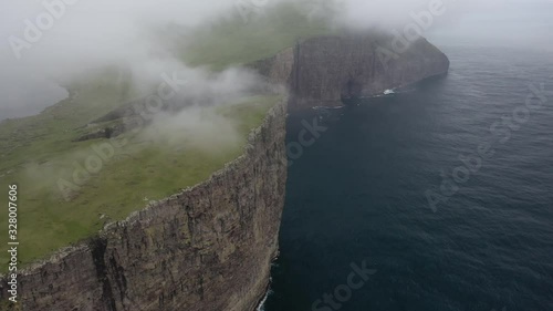 Aerial flight above tall steep Faroe Islands sea cliffs, drone panoramic