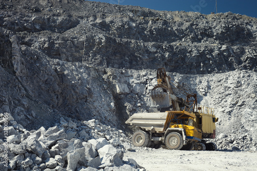 Mining excavator and heavy mining truck in a quarry for the extraction of limestone on the background of rocky terrain in sunny weather, close-up. photo