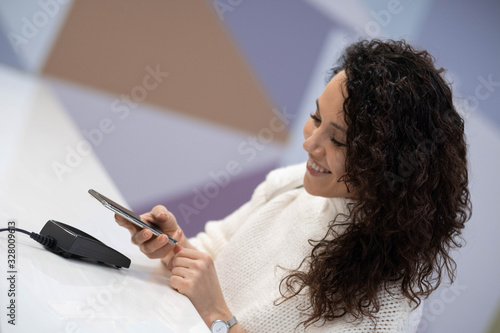 A cheerful beautiful woman pays for a service in a medical clinic using her phone