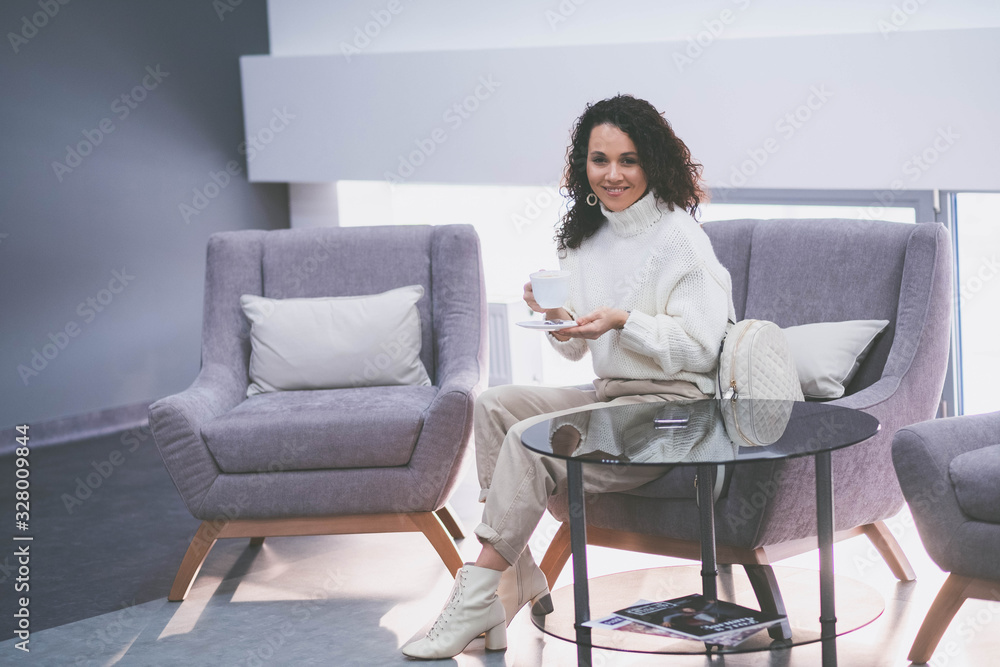 A serious beautiful woman is drinking tea in the clinic waiting for a dentist appointment A serious beautiful woman is drinking tea in the clinic waiting for a dentist appointment
