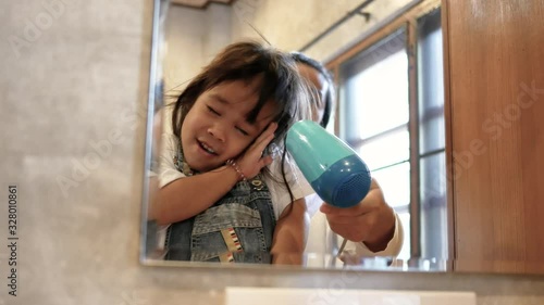 Young cute little girl standinng on chair in morning and smile looking at mirror when mother uses a hair dryer to dry. photo