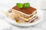 Traditional italian dessert tiramisu on a white plate on a marble table. Close-up. Selective focus