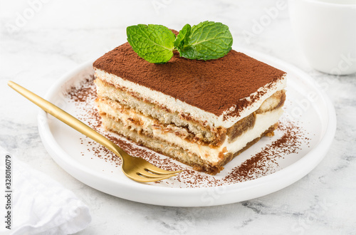 Traditional italian dessert tiramisu on a white plate on a marble table. Close-up. Selective focus photo