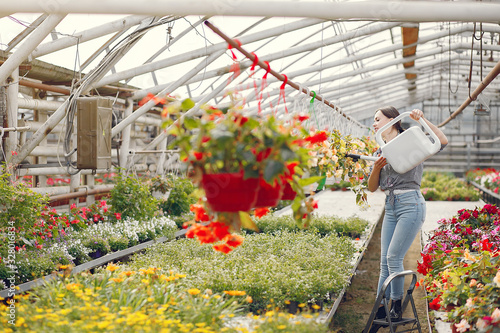 Woman in a greenhouse. Worker pours flowerpoots. Girl in a blue shirt. photo