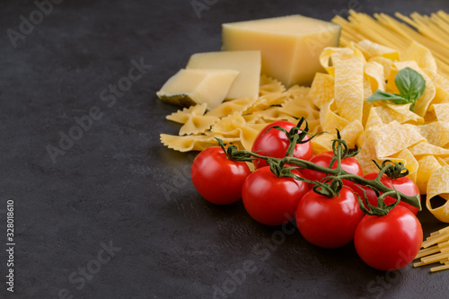 Different types of pasta, tomatoes and parmesan cheese on black stone background. Concept of italian food