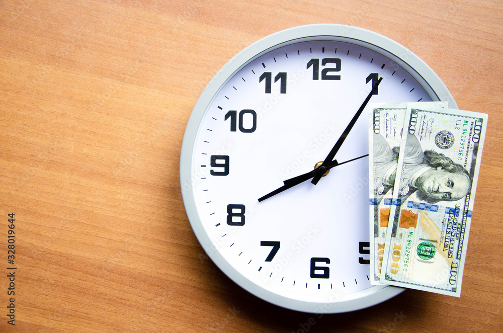 Analog clock and dollars on a wooden background. Banknotes are on the clock and next. Macro. Top and side view. The clock is 20:05, 08:05. Copy Space Analog clock and dollars on a wooden background. Banknotes are on the clock and next. Macro. Top and side view. The clock is 20:05, 08:05. Copy Space