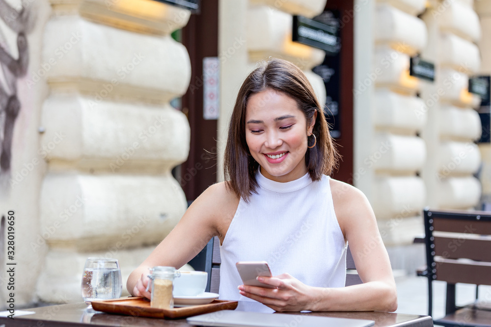 Smiling Asian woman drinking coffee and using her mobile phone. Satisfied female enjoying cup of coffee. Close up portrait of beautiful girl drinking coffee from a white mug in the coffee shop Smiling Asian woman drinking coffee and using her mobile phone. Satisfied female enjoying cup of coffee. Close up portrait of beautiful girl drinking coffee from a white mug in the coffee shop