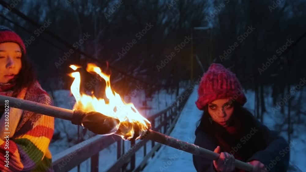 Two young women fighting with fired torches standing in winter forest Two young women fighting with fired torches standing in winter forest