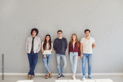 Group of young people in casual clothes smiling while standing against gray background. photo