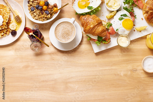 Brunch flatlay on wooden table. Healthy sunday breakfast with croissants, waffles, granola and sandwiches. Banner composition with copy space