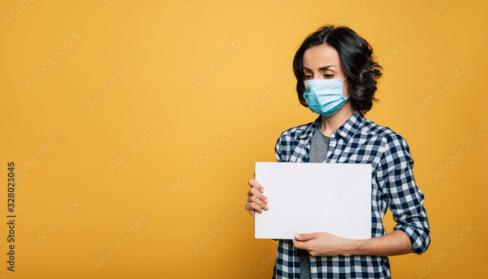 Young serious woman in a protective medical mask shows the blank board on camera. Woman wearing face mask because of Air pollution or virus epidemic. Young serious woman in a protective medical mask shows the blank board on camera. Woman wearing face mask because of Air pollution or virus epidemic.