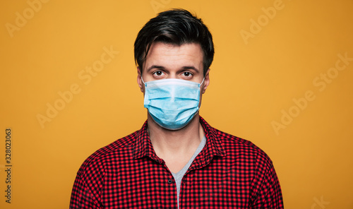 Young serious man in a protective medical mask looks on camera. Man wearing face mask because of Air pollution or virus epidemic.