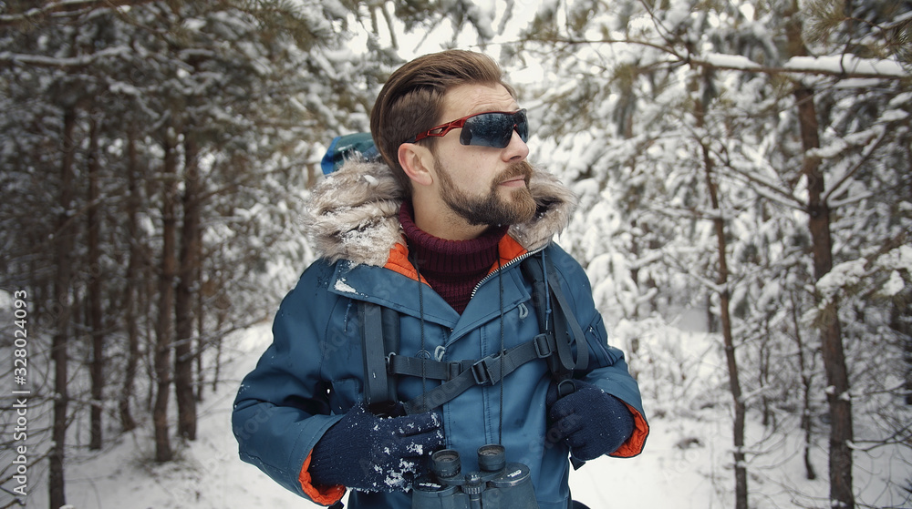 Portrait of mature bearded male in hiking sunglasses walking in snow-covered forest, front view Portrait of mature bearded male in hiking sunglasses walking in snow-covered forest, front view