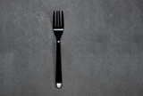 simple clean black plastic fork on a flat clean gray background with a hard shadow. The minimalist monochrome photo of dishes.
