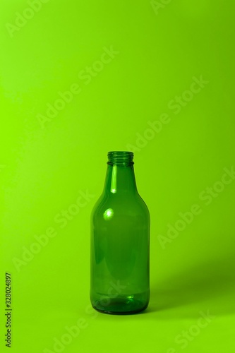 Small empty green glass bottle without cover and label on bright neon green background. Can be used as mock up for juice or beer.